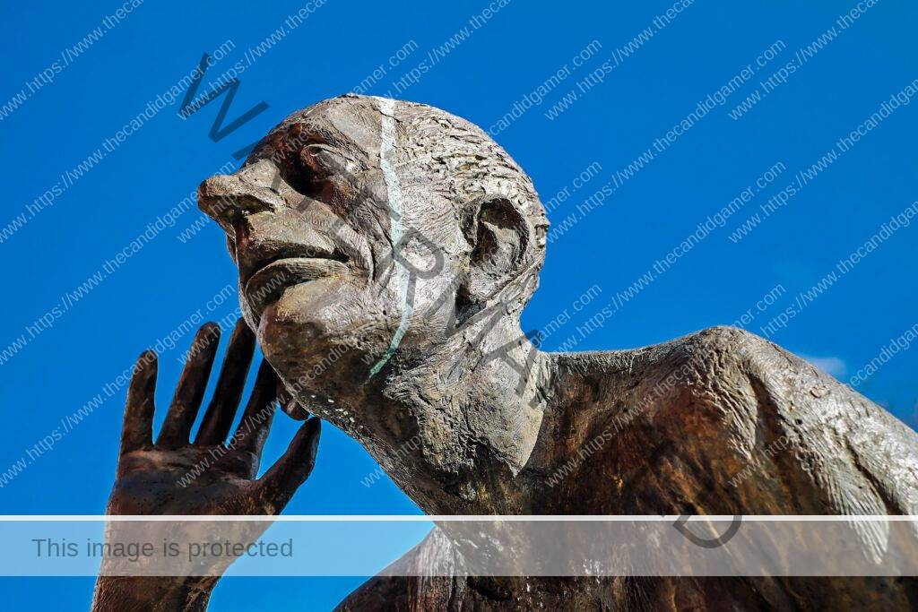 A statue of a man is pictured. The man holds a hand by his ear, as though to listen. Bird droppings trail off its head.