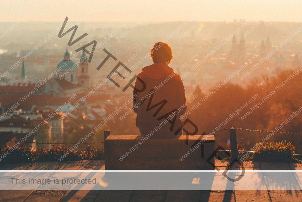 A young man sits on a bench, overlooking the city below.
